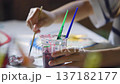 Close up of children's hands painting with brushes and colorful watercolors in a plastic cup, creative art activity for kids at home or school. 137182177