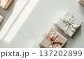 Presents are arranged on a light surface. The gifts are in neutral colours and have ribbons. Soft shadows are created by sunlight coming in. The setting shows a simple and clean arrangement 137202899
