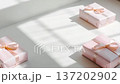 Pink gift boxes are arranged on a bright surface. Soft sunlight creates shadows across the area. The boxes feature ribbons and are ready for giving 137202902