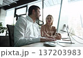 Two people are sitting at a desk with a computer monitor in front of them 137203983