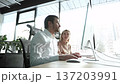 A man and a woman are sitting at a desk in front of a computer monitor 137203991