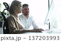 A man and a woman are sitting at a desk with a computer monitor in front of them 137203993