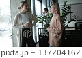 Two women are talking in a room with a potted plant in the background 137204162