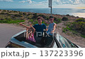 A cheerful family with children is driving a convertible car along the ocean and enjoying life and the sunny day while leaning out of the roof of the car 137223396