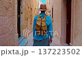 A female tourist in a hat and with a backpack walks along the traditional narrow old streets in Mdina, Malta 137223502