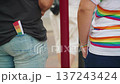Accessories and clothing with rainbow shades on unrecognizable persons. T-shirt with rainbow stripes, folded fan in back pocket of jeans adorns people before parade and lgbtq celebration in city. 137243424