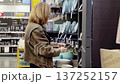 Woman examines various plates in a supermarket, thoughtfully considering her choices among an array of crockery items neatly arranged on the shelves 137252157