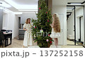Contemporary apartment interior showing mother and daughter decorating pine tree, hanging colorful ornaments and sharing cheerful holiday moment together 137252158