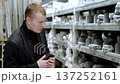 Man in an electrical goods store. Man wearing casual clothing is comparing plumbing supplies in a home improvement store. He is holding a smartphone and looking at the products 137252161