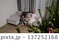 Family members sitting near sparkling christmas tree, cuddling on home sofa, sharing warm moment of connection and festive holiday togetherness 137252168