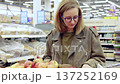 Young woman wearing glasses inspects apples in a supermarket. Picking up the fruit, she smells and examines them for freshness and quality before making her selection 137252169
