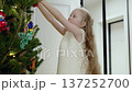 Festive holiday scene portraying young girl decorating pine tree, gradually joining father while creating warm seasonal family moment 137252700