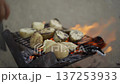 Potatoes are being grilled on a metal grate above a lively fire, capturing the essence of outdoor cooking. The flames and rustic setup evoke warmth and a sense of culinary adventure 137253933