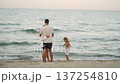 A loving family spends quality time by the sea, embracing tranquility and togetherness. The parents share a tender moment as their child explores the sandy beach under a soft evening sky 137254810