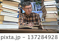 Focused man reading between tall stacks of books at home desk 137284928