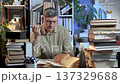 Mature man studying and reading books at desk in home library 137329688