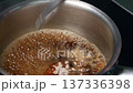Dark brown liquid simmers in stainless steel pot as flour is added and whisked to create a smooth chocolate demi-glace sauce on a stovetop 137336398