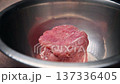 Raw beef steak resting in a stainless steel bowl with water, showcasing the texture and color of the meat in a kitchen setting, preparing for cooking 137336405