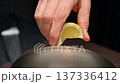 Hand squeezing lemon into metal bowl with salmon meat and chopped vegetables and herbs 137336412
