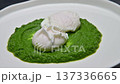 Poached eggs placed on vibrant green puree in a white dish, showcasing a culinary presentation with smooth texture and contrasting colors on a dark surface 137336665