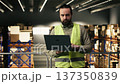 Industrial employee working on laptop in warehouse logistics center, checking delivery and transportation details. Managing cargo and logistics for order fulfillment and inventory control. 137350839