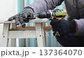Process of cutting metal with cutting disc on cordless screwdriver in garage conditions close up. Person in protective gloves makes groove when assembling structures in cold hangar. 137364070