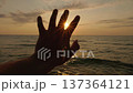 Silhouette of hand reaching toward sunrise over sea horizon at golden morning light 137364121