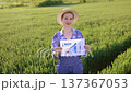 A smiling woman in overalls and a straw hat stands in a green field holding a paper with a bar graph and an upward trending arrow 137367053