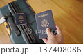 Hand holding United States passport above rolling travel bag with second passport preparing for trip 137408086