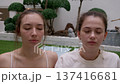 Close up portrait shows two young women meditating with closed eyes in zen courtyard garden. Relaxed faces and soft expressions convey deep inner peace and mindfulness. 137416681
