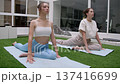 Fit girls perform forward bend stretch on blue mats over green grass surface. 137416699