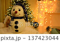 a beautiful snowman in a blue cap and with a kind smile against the background of a garland. toy for gift or room decoration for New Year or Christmas. warmth and kindness 137423044