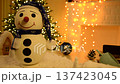 a beautiful snowman in a blue cap and with a kind smile against the background of a garland. toy for gift or room decoration for New Year or Christmas. warmth and kindness 137423045