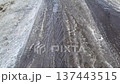 A trickle of dirty meltwater flows over the asphalt and dirty snow, following the trail left by the car on the road. 137443515