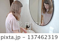 Woman washes hands at bathroom sink while looking down near mirror 137462319