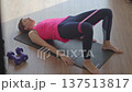 Woman in sportswear performs glute bridge on fitness mat with resistance band around legs 137513817