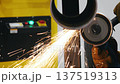 Worker cutting metal pipe with angle grinder producing sparks. 137519313