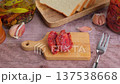 Sun-dried tomatoes in olive oil on a mini board with homemade bread in a rustic style. Traditional home cooking. A woman puts tomatoes on a board. Selective focus, close-up. 137538668