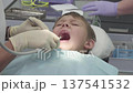 Dentist examines a boy's mouth in a dental clinic. The boy lies on the chair while the dentist uses tools for the checkup process 137541532