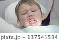 Funny boy sits in a dental chair showing a chipped tooth. He makes funny faces while the dentist examines him 137541534