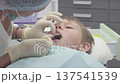 Dentist treats a boy with a chipped tooth. The dentist carefully applies a special glue to the chipped area to attach a broken tooth fragment 137541539