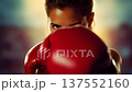 Intense close-up of a determined female boxer in red gloves, focused and ready for the fight. The athlete's strong gaze embodies power, training, and motivation. 137552160