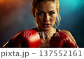 Strong focused female boxer in red gloves throwing a powerful punch towards the camera, symbolizing strength, confidence, determination, self defense and women empowerment. 137552161