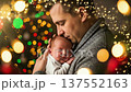 A loving father gently holds his sleeping newborn baby in front of a festive, blurred Christmas tree with beautiful bokeh lights. Capturing the tender bond and joy of family during the holiday season. 137552163