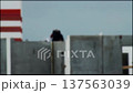 Worker performs welding activity on concrete wall at construction site, bright sparks visible against cloudy sky, industrial scene with striped tower part 137563039