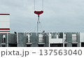 Construction workers on top of partially built residential apartment building installing concrete panels with large red crane hook in cloudy sky background. 137563040