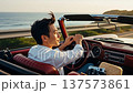 Asian man driving vintage convertible car along scenic coastal highway during golden hour sunset 137573861