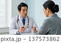 Asian male doctor in white coat consulting with female patient in modern medical office during healthcare appointment 137573862