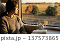 Young Asian woman reading book while traveling by train during golden hour sunset with coffee cup and countryside view through window 137573865
