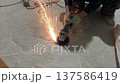 Worker using an angle grinder on a concrete floor with sparks flying 137586419